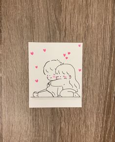 a sticker with a drawing of two people hugging each other on a wooden surface