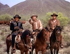 three men in cowboy hats are riding horses