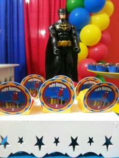 a batman birthday party with cupcakes, cake and decorations on a table in front of balloons