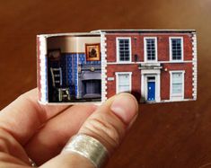 a hand holding a miniature model of a red brick building with blue doors and windows