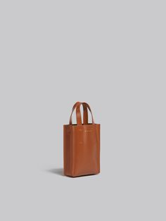 North/South tote bag, nano size, in calf leather with internal slot pocket. Leather top handles. Detachable and adjustable recycled tape shoulder strap with Marni lettering. Gold hardware. Gold printed logo outside. Made in Italy. Everyday Calf Leather Rectangular Satchel, Tan Leather Box Bag For Shopping, Rectangular Calf Leather Bucket Bag With Handle Drop, Business Rectangular Calf Leather Bucket Bag, Square Leather Box Bag With Dust Bag, Classic Rectangular Calf Leather Bucket Bag, Square Leather Bucket Bag With Dust Bag, Tan Leather Box Bag With Removable Pouch, Leather Tan Box Bag For Everyday Use