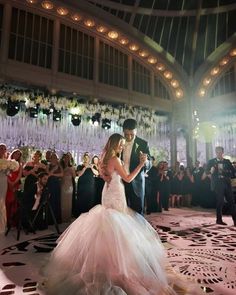 a bride and groom are dancing in front of their guests at a wedding reception with chandeliers hanging from the ceiling