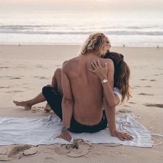 a man and woman sitting on top of a beach next to the ocean at sunset