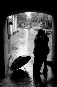 a man and woman kissing under an umbrella in the rain on a brick walkway next to a river