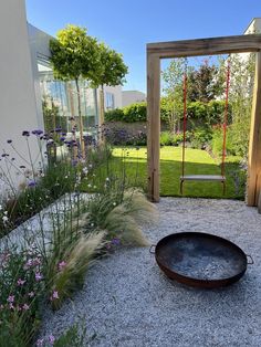 a garden with gravel and flowers in front of a swing set, surrounded by plants