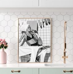 a kitchen with white cabinets and pink vases on the countertop next to a framed photograph