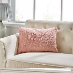 a pink pillow sitting on top of a white chair next to a lamp and window