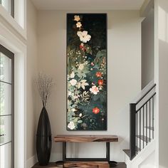 a painting hanging on the wall next to a wooden bench and vase with flowers in it