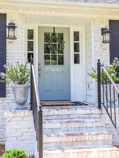 the front door of a white brick house with blue shutters and potted plants