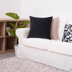 a white couch with two black pillows and a bookcase in the corner behind it