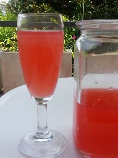 a glass filled with liquid sitting on top of a white table next to a jar