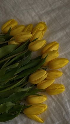 a bunch of yellow flowers laying on top of a white cloth covered tablecloth with green leaves