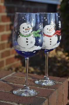 two wine glasses with snowmen painted on them are sitting on a brick ledge outside