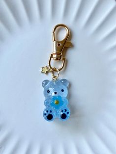 a blue teddy bear keychain sitting on top of a white plate next to a gold star