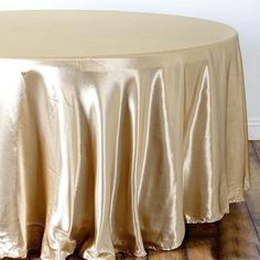 a round table covered with a gold satin tablecloth next to a white wall and wooden floor