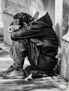 a man sitting on the ground with his head in his hands and holding a cup