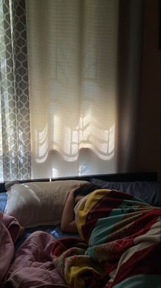 an unmade bed in front of a window with curtains