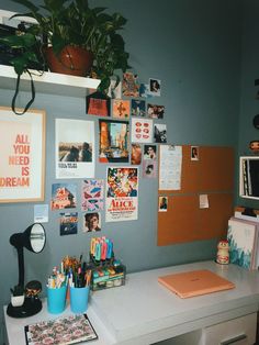 a desk with many pictures on the wall above it and a plant in a pot