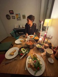 a woman sitting at a table with plates of food and candles in front of her