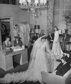 a woman in a wedding dress and veil walking through a room with other people sitting around