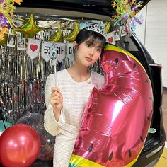 a woman holding a balloon in front of a car with balloons and streamers on the back