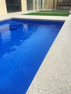 a blue swimming pool in front of a house with artificial grass and an artificial lawn