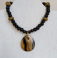 I've used the Japanese  technique mokume gane to create this polymer clay pendant. It comprises gold, white and black polymer clay. The pendant has been teamed with black wooden beads and golden spacer beads. The necklace is closed with a lobster claw lock and extends to 48cm if using the extender chain. The pendant measures 4.2 x 3.5cm. For more jewellery in similar colours, see the polymer clay section. Gold Pendant Necklace In Polymer Clay, Gold Polymer Clay Pendant Necklace, Unique Gold Polymer Clay Necklace, Gold Carved Beads Jewelry, Gold Carved Round Beads Jewelry, Gold Carved Round Pendant Necklace, Artisan Carved Necklaces As A Gift, Brown Carved Round Pendant Necklace, Spiritual Polymer Clay Pendant Necklace