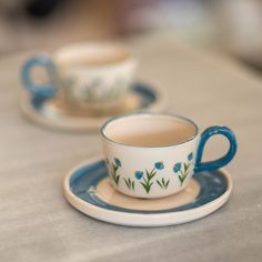 two tea cups and saucers sitting on a table with blue trim around the edges