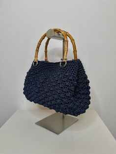 a crocheted blue purse sitting on top of a metal stand next to a white wall