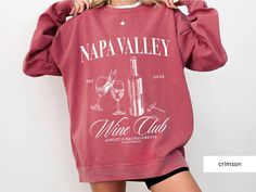 a woman in a red sweatshirt holding up her wine bottle and glass sweater that says napa valley