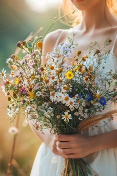 a woman holding a bouquet of wildflowers and daisies in her hands,