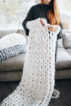 a woman is holding up a giant chunky knitted blanket in front of a couch