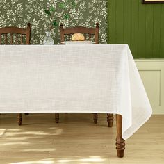 a dining room table with two chairs and a white tablecloth on it in front of green wallpaper