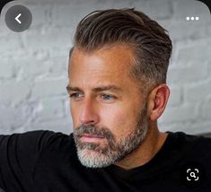 a man with grey hair and beard wearing a black t - shirt looking at the camera