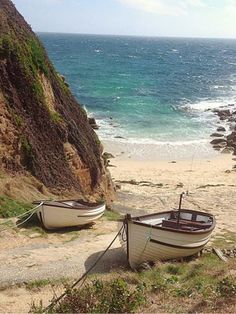 two boats sitting on the beach next to each other near the water's edge