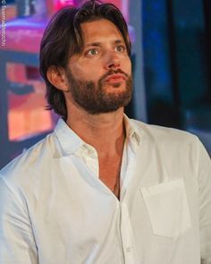 a man with long hair and beard wearing a white shirt looks up to the sky