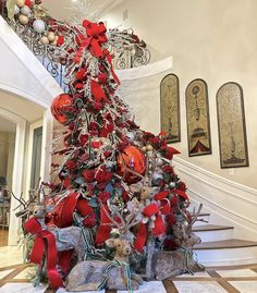 a decorated christmas tree with red and silver ornaments on it in the middle of a foyer