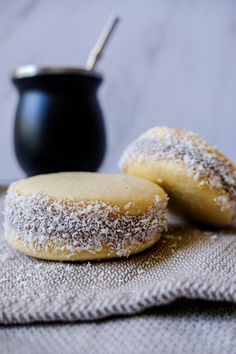 two powdered sugar donuts sitting on top of a cloth next to a black pot