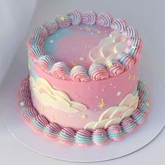 there is a pink and blue cake with clouds on the top that has rainbow icing