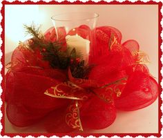 a candle is sitting in a red mesh wreath with gold trimmings on it