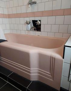 a pink bath tub sitting on top of a black tile floor