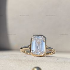 a ring with an emerald cut diamond in it sitting on top of a white surface