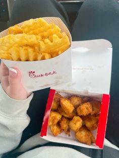 a person is holding up a box of french fries in their hand while sitting on an airplane