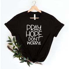 "Are you looking for a stylish and meaningful shirt? Look no further than the Pray Hope Don't Worry shirt! This eye-catching shirt features a bold graphic of the words \"Pray Hope Don't Worry\" in an elegant script font against a classic black background. It's the perfect way to show off your faith and spread positive vibes everywhere you go. This classic style faith shirt features a soft cotton material that is lightweight and breathable, making it comfortable to wear all day. The shirt also ha Cheap Business Shirt Solid, Cheap Baggy Black Tops, Inspirational Black Pre-shrunk Top, Inspirational Black Tops With Text Print, Inspirational Text Print Black Tops, Inspirational Black Cotton Tops, Friendship Shirts, Pray Shirt, Pray More Worry Less