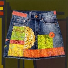 This awesome fringed jeans skirt reminds me of a sunny day. It's embellished with 8 different batik fabrics in glorious shades of orange and green, plus a bit of Kantha embroidery primitive American embroidery, vintage crochet doily, and a crochet flower. There's an orange-and-yellow strip of checkered fabreic along the waistline. The stitching is deliberately primitive for a clearly handmade look. The skirt itself is tagged as a size 5. Waistline measures 28 1/2", and the length (measured along the side seam from top of waistband to fringe) is 14". The mid-weight denim has 1% spandex for just a little stretch.  Despite the fact that this skirt is highly embellished, I am careful to create a design that does not obstruct the pockets, the zipper fly, the belt loops - everything is comfortab Fringed Jeans, Denim Upcycle, American Embroidery, Embroidery Crochet, Art Jeans, Upcycled Jeans, Jean Skirts, Diy Denim, Fashion Archive