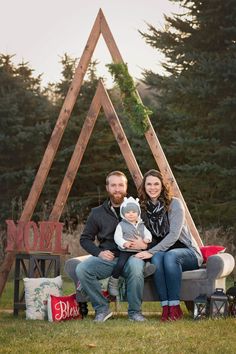 a man and woman sitting on a bench holding a baby in front of a teepeel