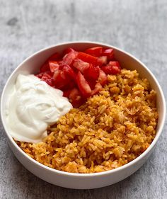 a bowl filled with rice, strawberries and yogurt next to a spoon