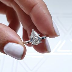 a woman's hand holding a ring with a pear shaped diamond on top of it