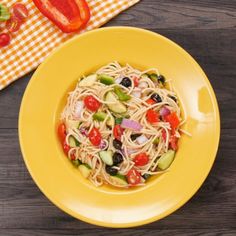 a yellow plate topped with pasta and veggies on top of a wooden table