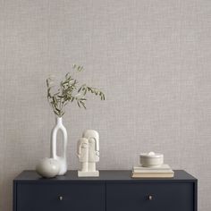 two white vases sitting on top of a black dresser next to a plant and books